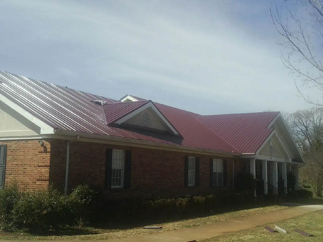 Red metal roof with gabled entries on a long brick building, from a Hail Damage Roof Repair job in Plainfield